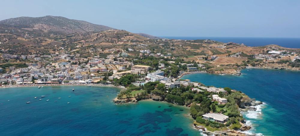 A stunning aerial view of Agia Pelagia, Crete, Greece, showcasing the coastal town, blue waters, and surrounding hills on a clear day. | Cheap Car Rental